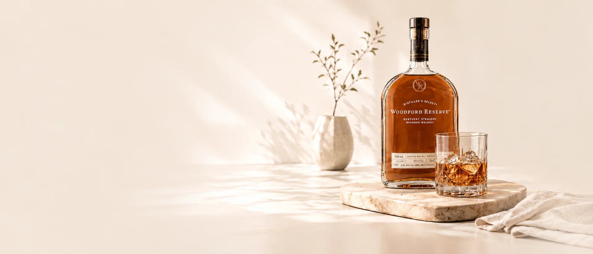 A bottle of Kentucky straight bourbon and a rocks glass on a stone board in soft daylight
